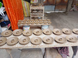 Multiple palo santo holders arranged on a worktable in a pottery workshop, with more clay pieces on stands in the background.